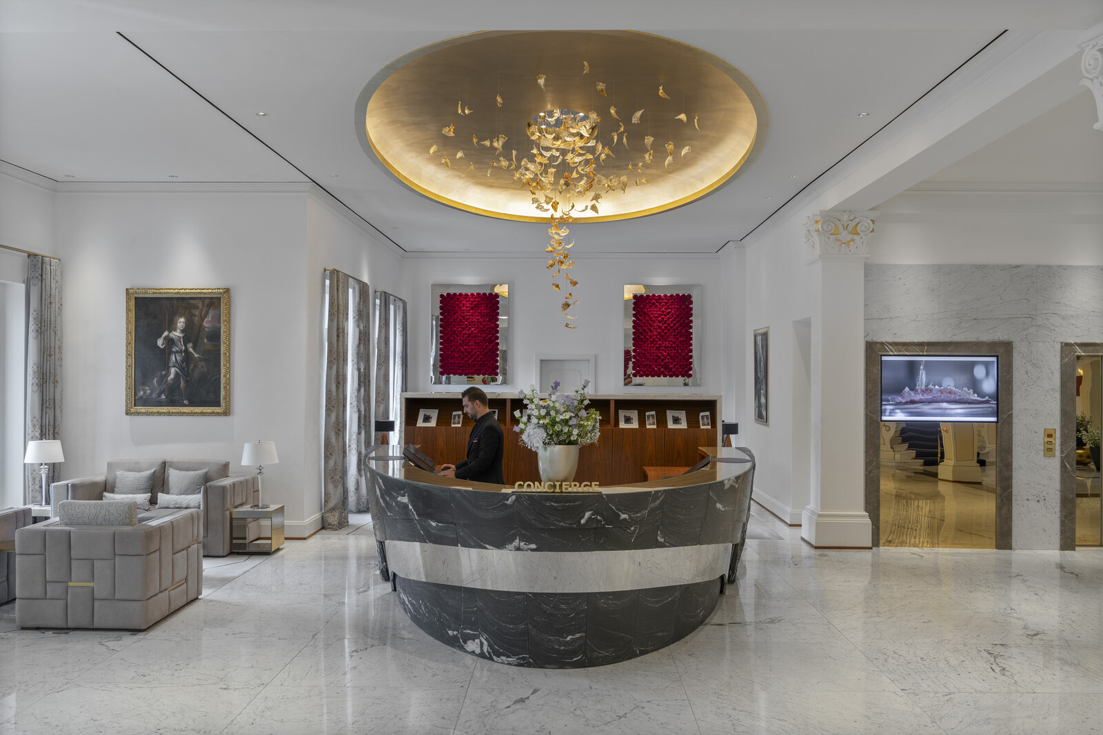 Luxuriöse Hotellobby des Grand Resort Bad Ragaz mit einem Concierge-Schalter aus Marmor, einem modernen Kronleuchter und eleganten Sitzgelegenheiten. Die Wände sind mit Kunstwerken geschmückt, die ein anspruchsvolles Ambiente schaffen.