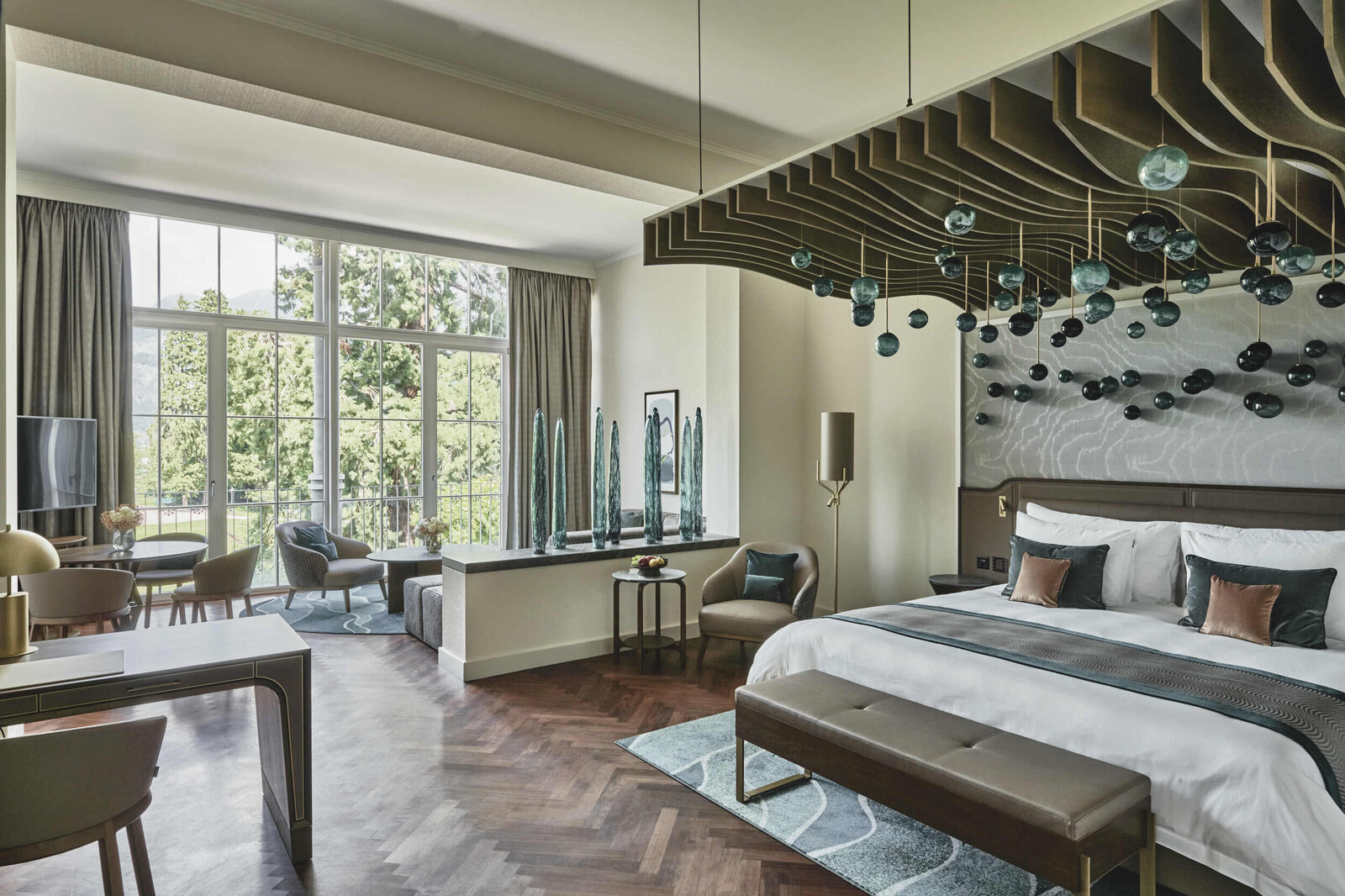 Blick in eine Deluxe Suite im Grand Hotel Hof Ragaz. Ein imposantes Himmelbett ist der Blickfang im Raum. In Richtung der Fenster befindet sich ein Wohnbereich, der optisch vom Raum getrennt wird.