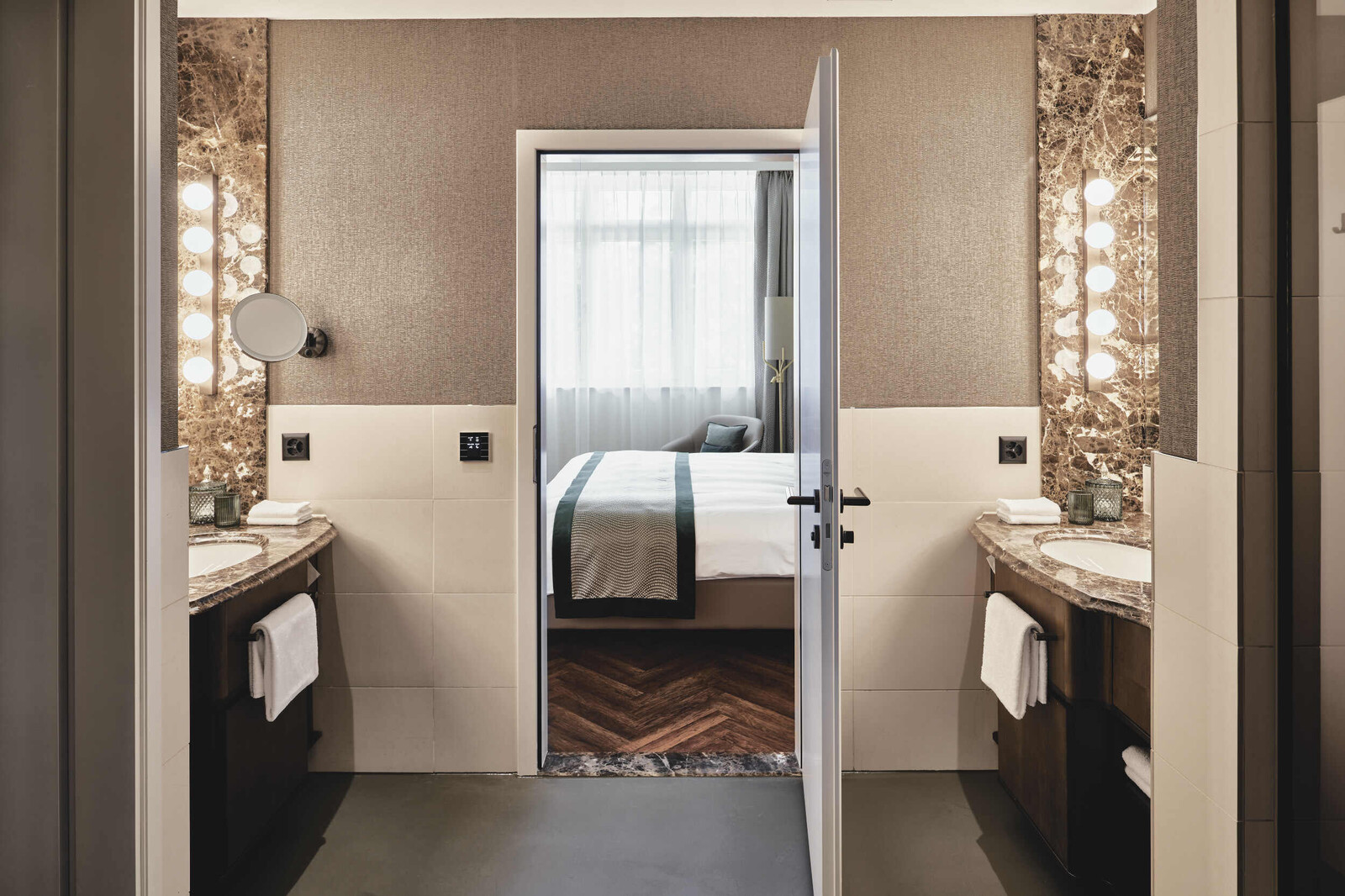 Blick vom Badezimmer in eine Grand Deluxe Suite. Auf beiden Seiten des Badezimmers befindet sich je ein Marmor-Waschtisch mit Spiegel und Lichtelementen.