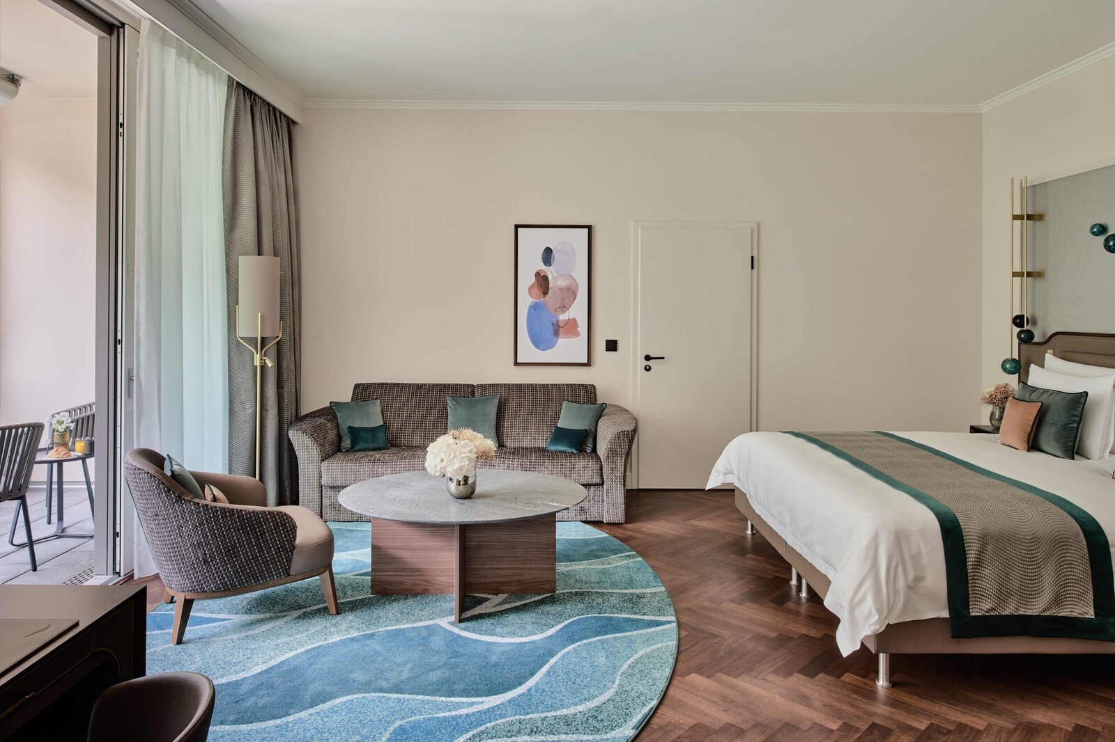Interior view of a Grand Deluxe Suite at the Grand Hotel Hof Ragaz. View of the bed as well as the living area of the room. Harmonious natural colors with blue and orange accents.
