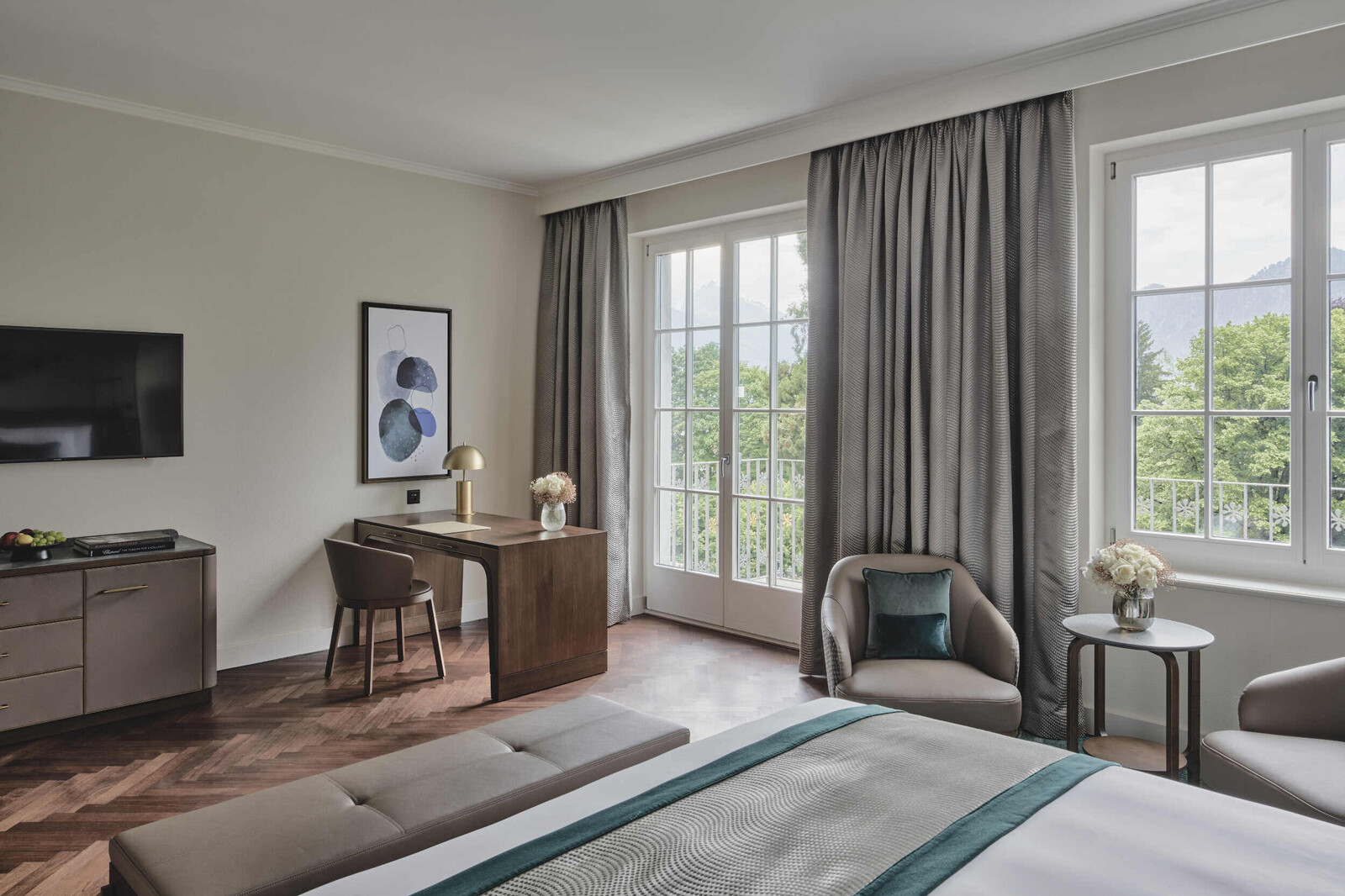 View from the bed of a Grand Deluxe room towards the windows. You can see part of the bed as well as a dresser, a desk and a sitting area.