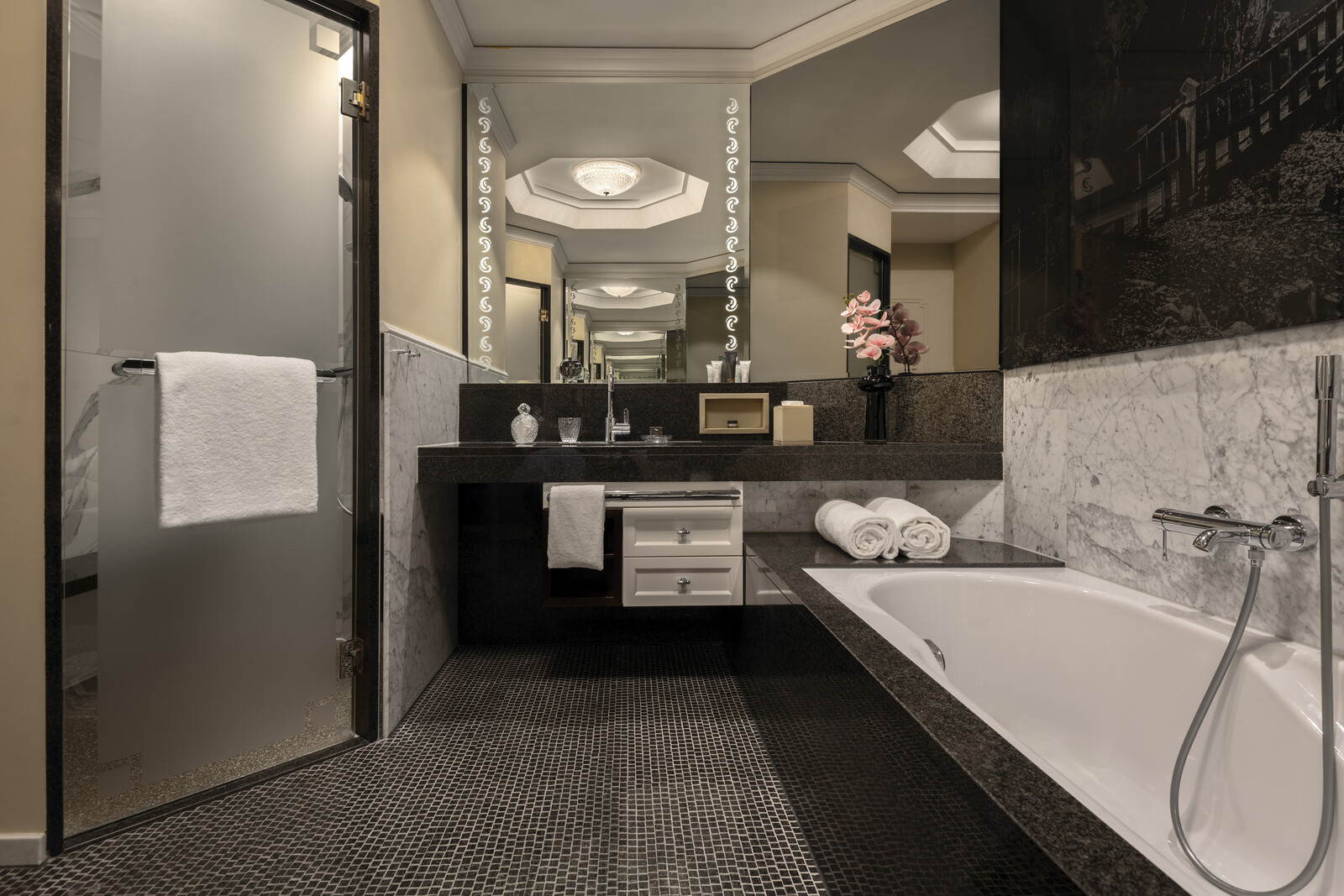 Luxurious bathroom with a frosted glass shower door, elegant black and white decor, large mirror, spacious bathtub, and soft lighting creating a serene ambiance.