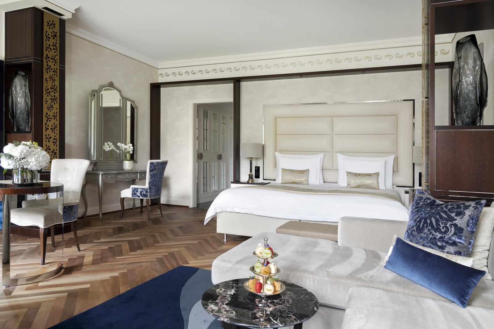 Luxurious Junior Suite of the Grand Hotel Quellenhof with a large bed with upholstered headboard, elegant chaise longue and blue velvet cushions. Bright and refined ambience.