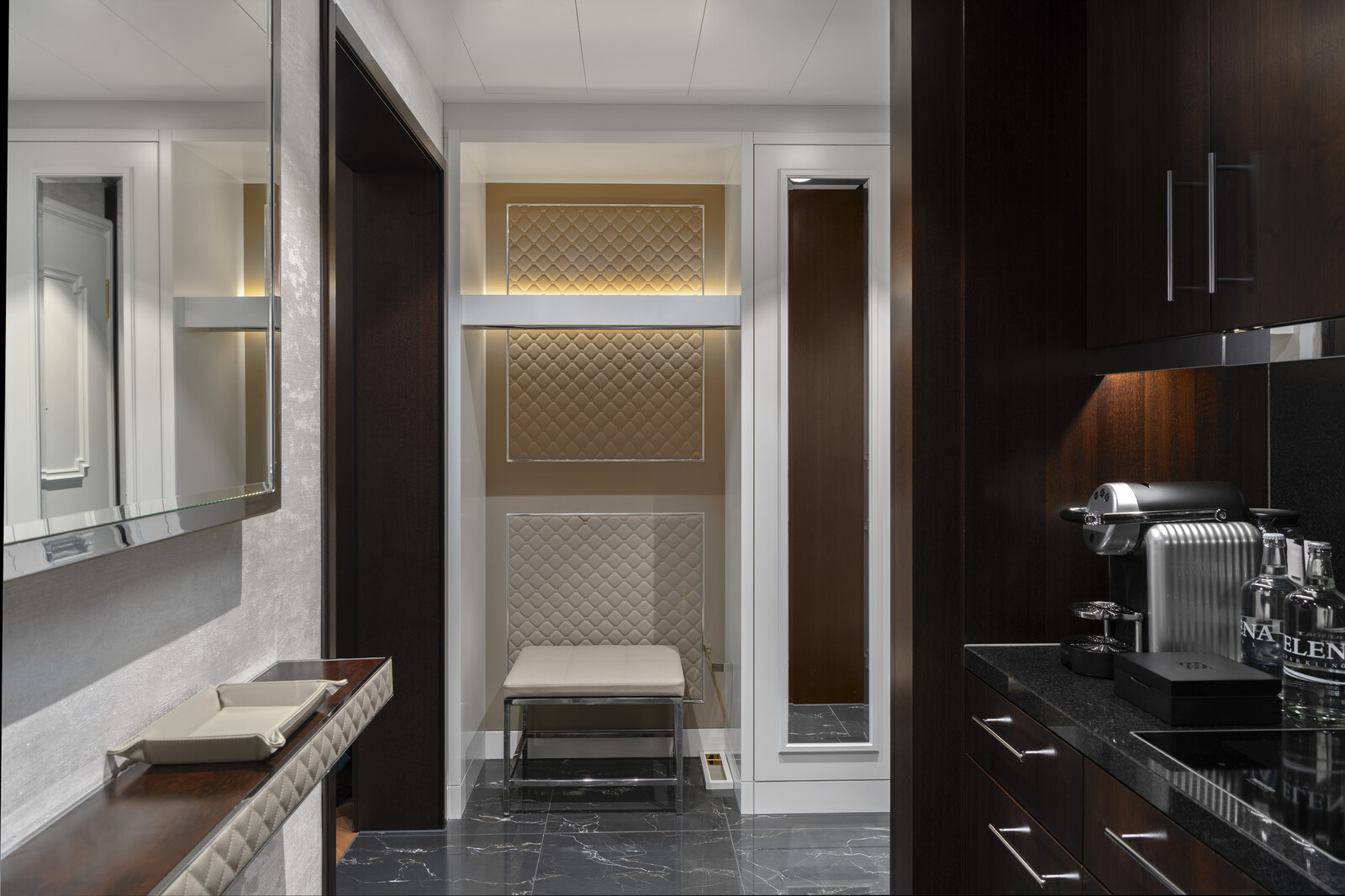 Elegant kitchenette with dark wood cabinets, glossy black countertops, and a modern coffee maker. Soft lighting highlights a sleek, minimalist design.