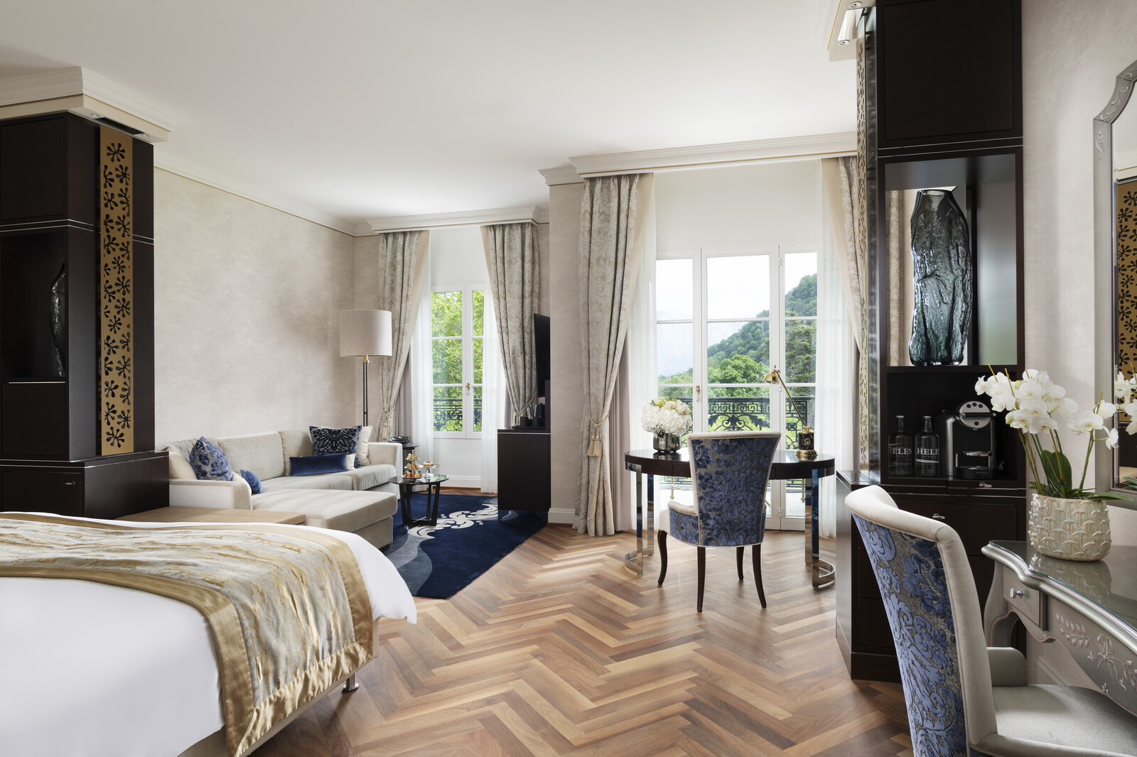 Luxuriöses Hotelzimmer mit elegantem Dekor, einem gemütlichen Bett, einem Plüschsofa, dunklen Holzmöbeln und raumhohen Fenstern mit Panoramablick.