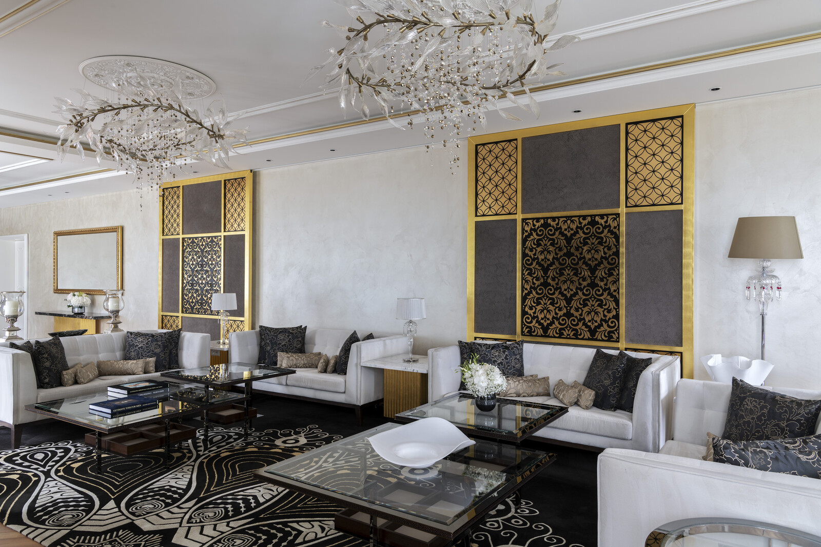 Luxurious living room of the King Suite with white sofas, ornate black and gold wall panels, intricate chandeliers, and patterned rugs. Sophisticated and elegant ambiance.