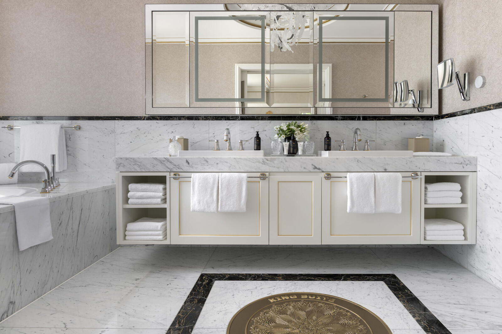 Luxurious bathroom with a marble bathtub and vanity, a large mirror, and a window revealing green trees outside. The ambiance is serene and elegant.