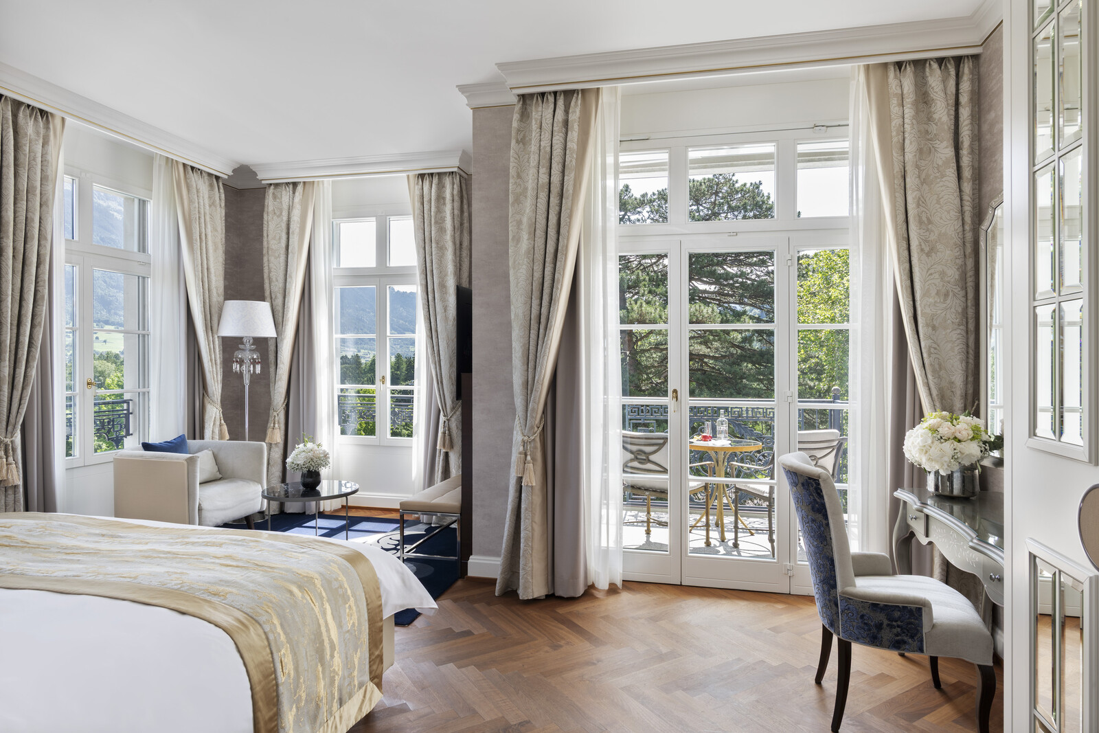 Elegantes Hotelzimmer mit großen Fenstern und transparenten Vorhängen, das einen Balkon mit Blick ins Grüne bietet. Mit stilvollen Möbeln und Blumendekor, das Ruhe ausstrahlt.