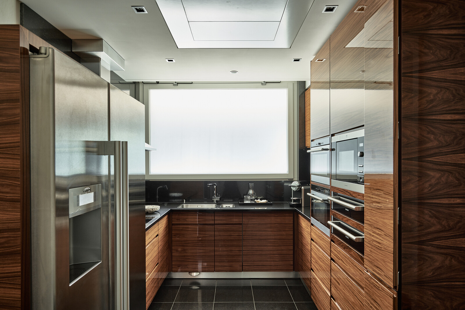 Moderne Küche mit eleganten, holzgetäfelten Schränken, Edelstahlgeräten und einem großen Milchglasfenster.