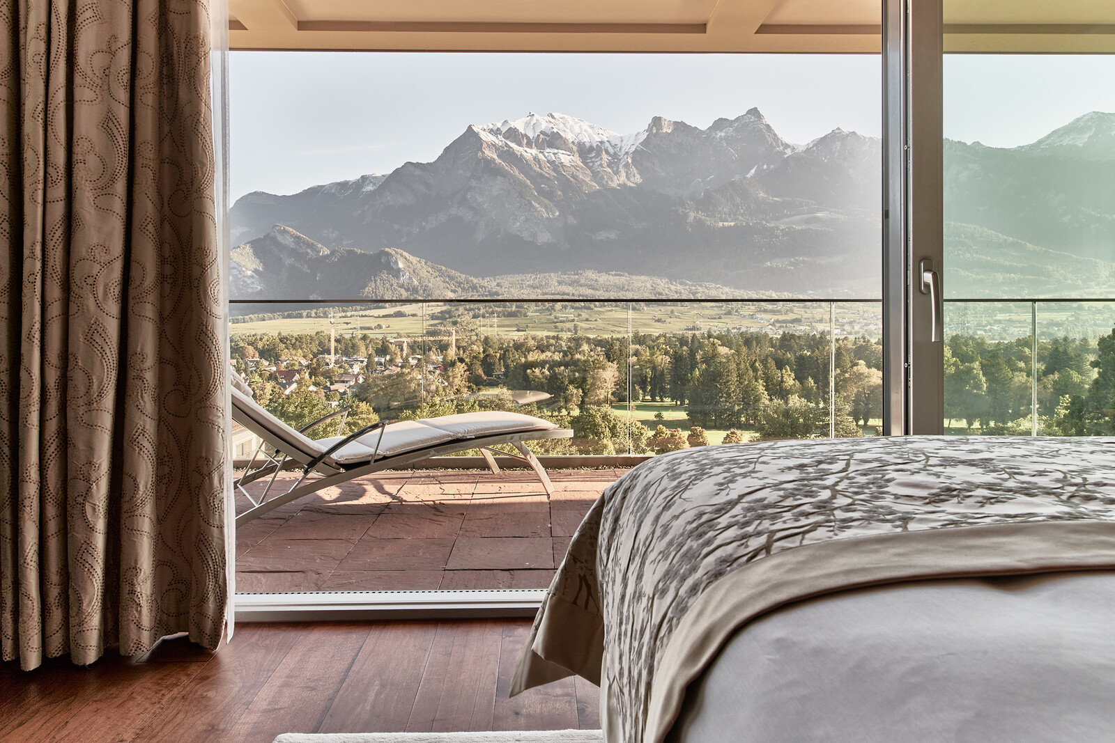 Luxuriöses Schlafzimmer mit großem Fenster und Blick auf einen Balkon und die Berge.