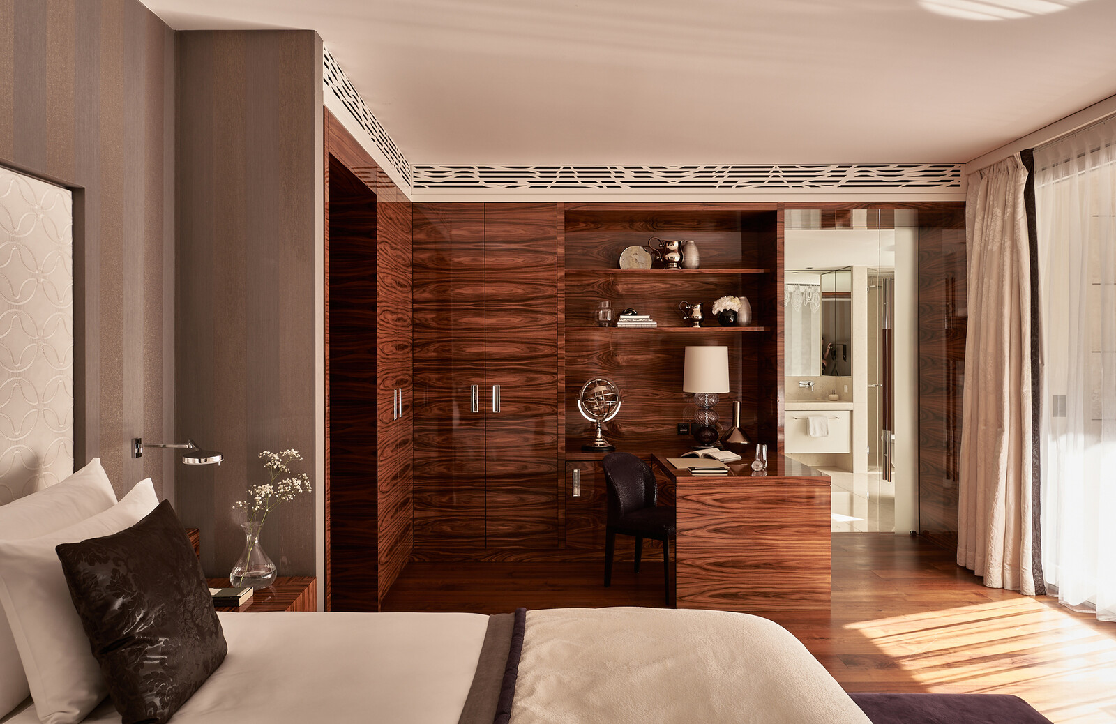 Luxuriöses Hotelzimmer mit holzgetäfelten Wänden, einem Schreibtisch mit einem Globus, einer Lampe und Büchern. Das Sonnenlicht fällt durch die transparenten Vorhänge und schafft ein warmes Ambiente.