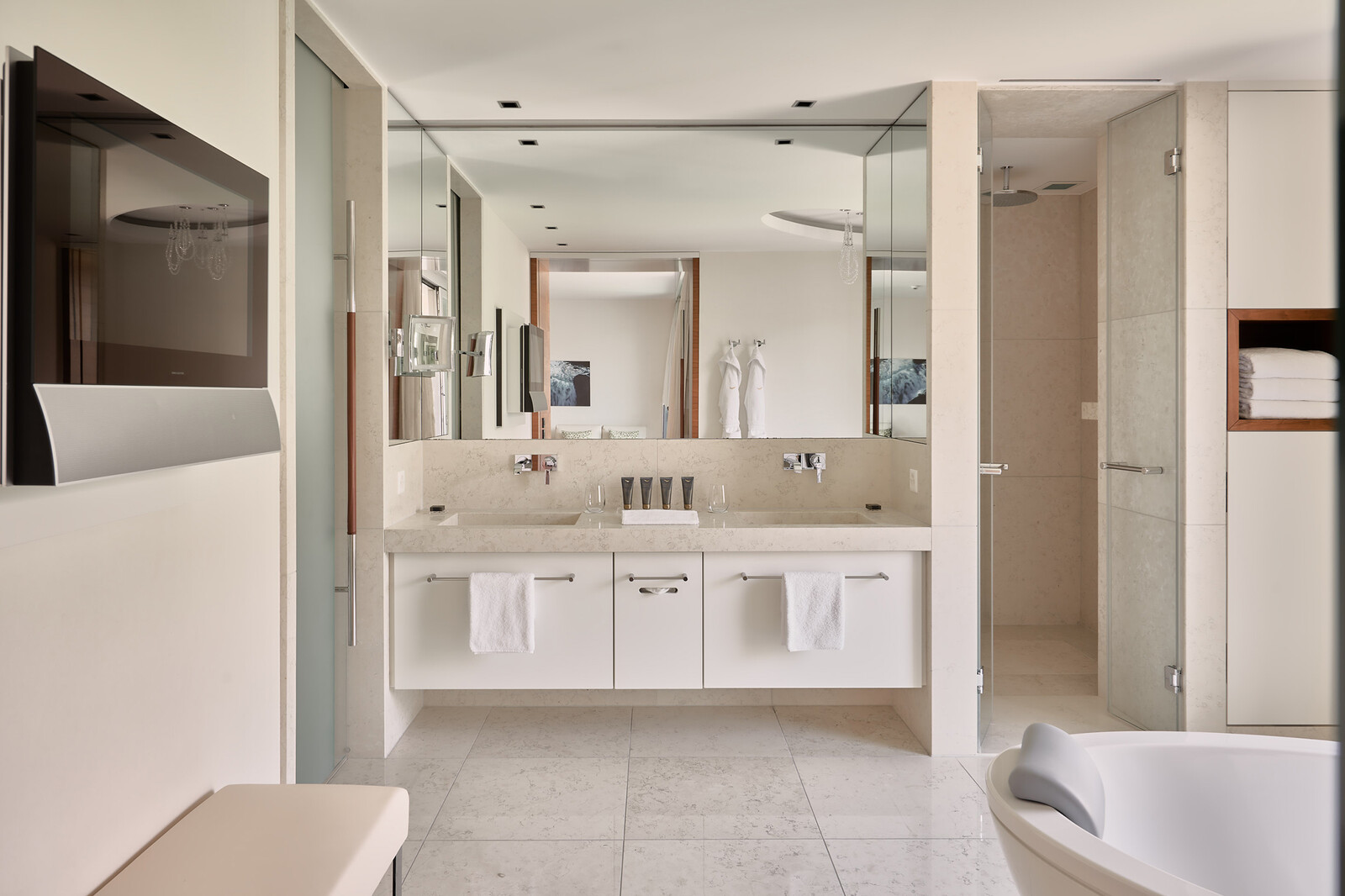 The modern bathroom of a Spa Loft Superior Suite in bright colors features a bathtub, a TV screen and a sink with a large mirror.