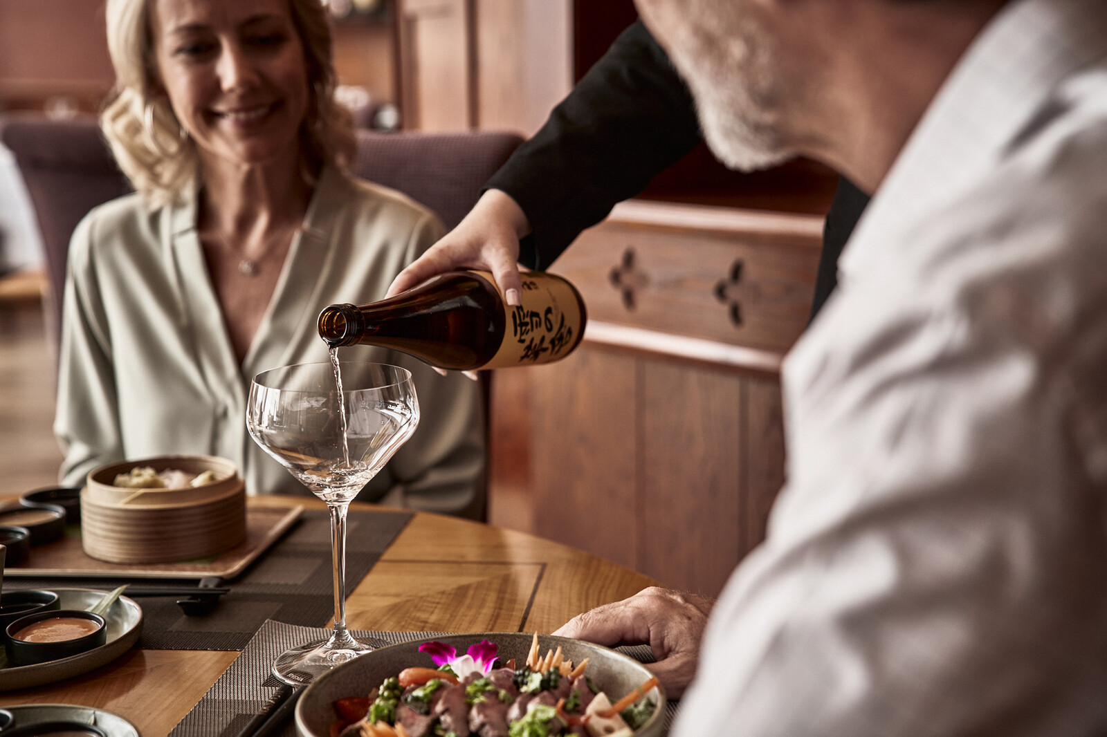 Die Sommelière bedient einen besetzten Tisch und schenkt Sake in ein Glas.