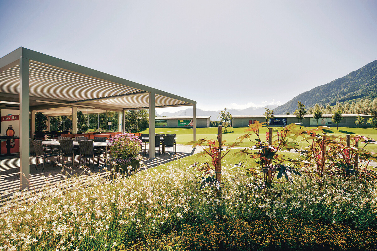 Die Terasse vom Bistro des Golf Clubs Heidiland umgeben vom Golfplatz und blühenden Blumen.