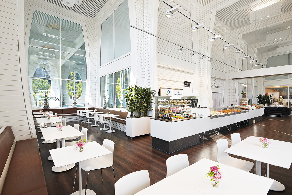 Das modern eingerichtete Café Therme des Grand Resorts Bad Ragaz mit weissen Tischen und Stühlen, einer Theke und einer grossen Fensterscheibe mit Blick in die Tamina Therme.