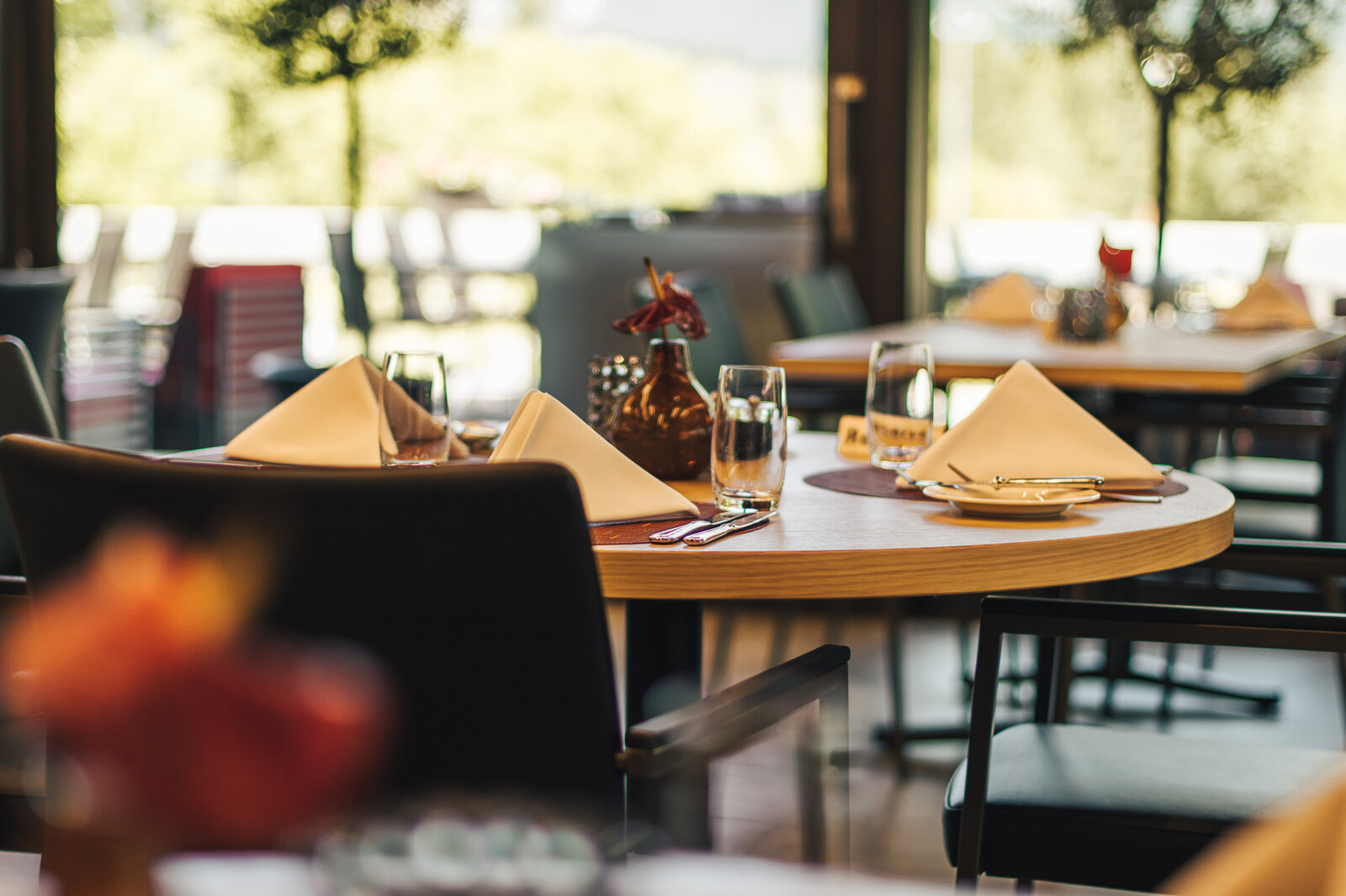 The table is already set with servings, glasses and cutlery and is waiting for the first guest. In the background you can see the windows that offer a view outside into the greenery. The Gladys Restaurant is the golf restaurant of the Hotel Grand Resort Bad Ragaz, a superior luxury resort in Switzerland.
