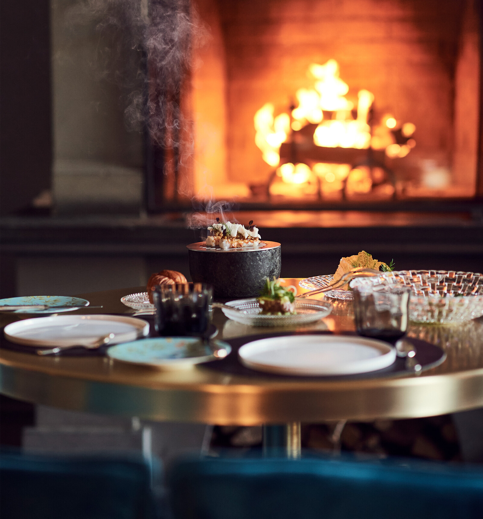 Ein gedeckter Tisch im Restaurant Igniv. Im Hintergrund lodert ein Feuer in einem offenen Kamin.