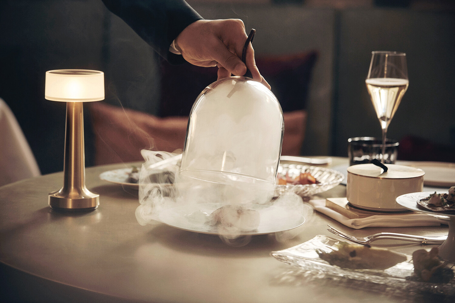 Der Kellner des Restaurant Igniv serviert einen Gang, in dem er die Glaskuppe hoch hält, aus der Dampf steigt und das Essen freigibt. Das Restaurant gehört zum Hotel Grand Resort Bad Ragaz, einem Superior Luxusresort in der Schweiz.