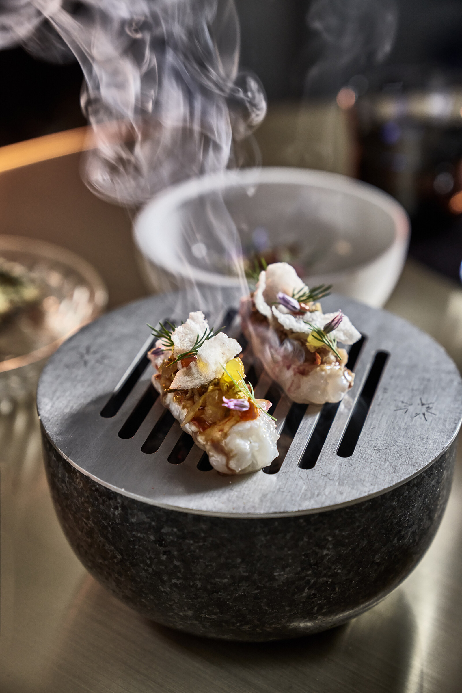 Der Gang kocht auf einer schwarzen, eisernen Platte, die sich auf einem Tisch befindet. Diese Nahaufnahme stammt aus dem Restaurant Igniv by Andreas Caminada, einem der Restaurants des Hotel Grand Resort Bad Ragaz, einem Superior Luxusresort in der Schweiz.