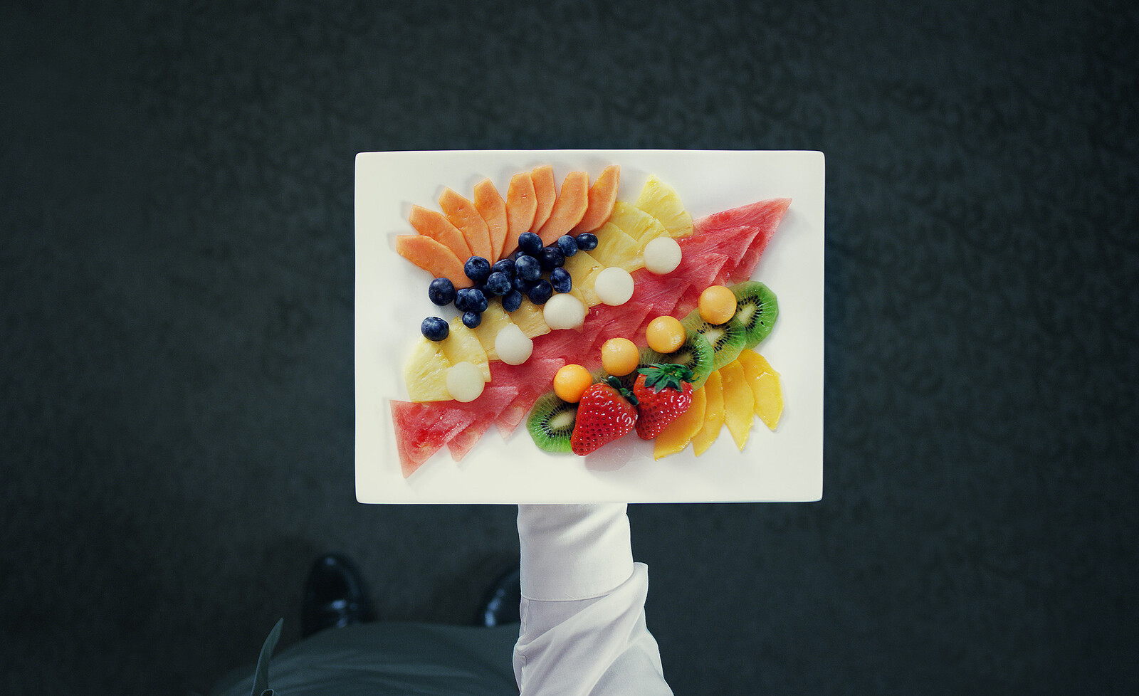 Ein rechteckiger weisser Teller mit stilvoll angerichtetem, aufgeschnittenen Obst.