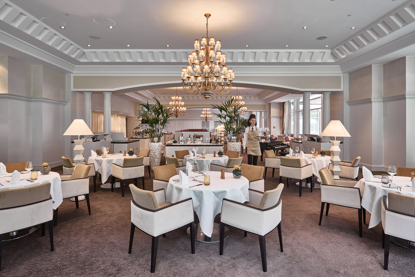 Eine Kellnerin trägt eine Flasche Wasser auf einem silbernen Tablett zu ihren Gästen im Restaurant Olives d'Or.