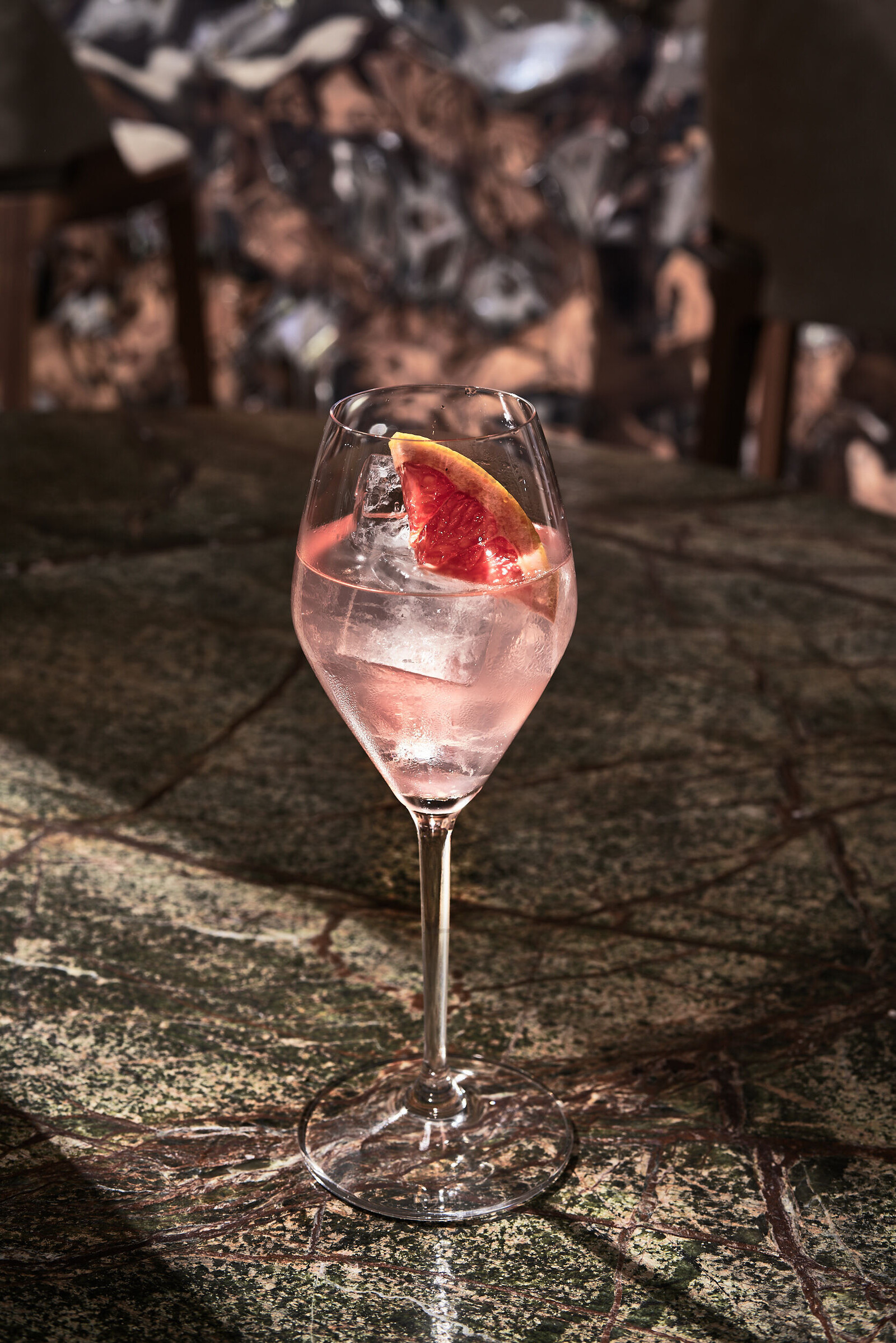 Ein roséfarbener Drink mit Eiswürfeln in einem Weinglass.