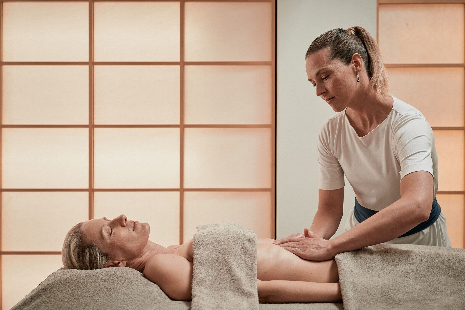 Eine Frau entspannt bei einer Chi Nei Tsang Massage auf einer Liege in einem der neutralen Behandlungsräume des Grand Resort Bad Ragaz.