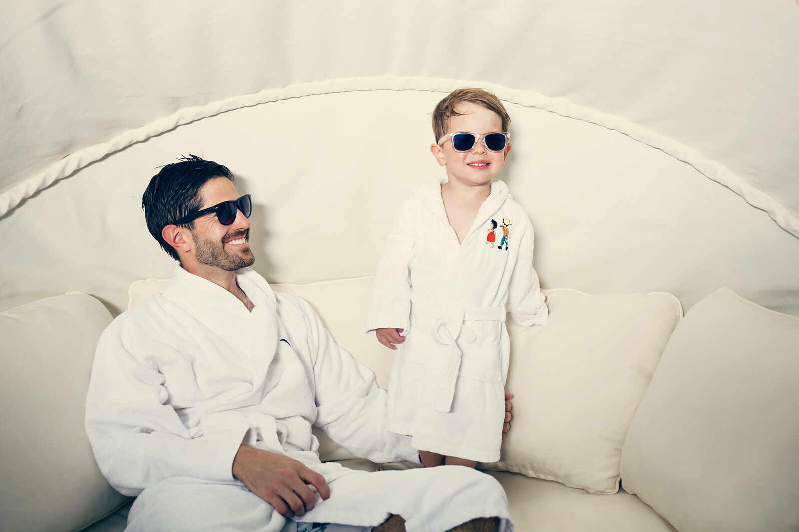 Vater und Sohn liegen im Grand Resort Bad Ragaz mit Sonnenbrille und Bademantel auf einem Sofa.