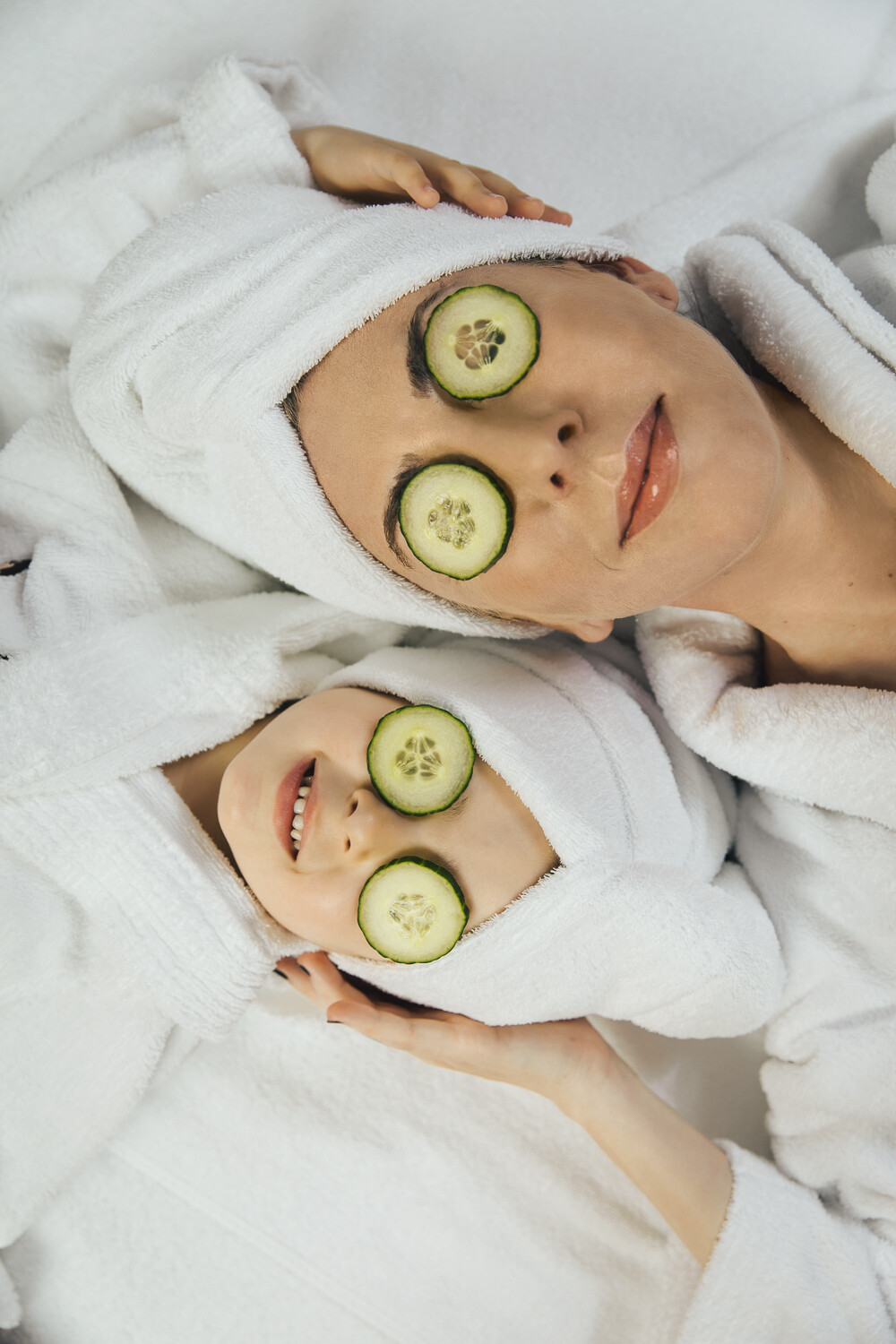 Mother and daughter relax in bathrobe and cucumber mask on face.