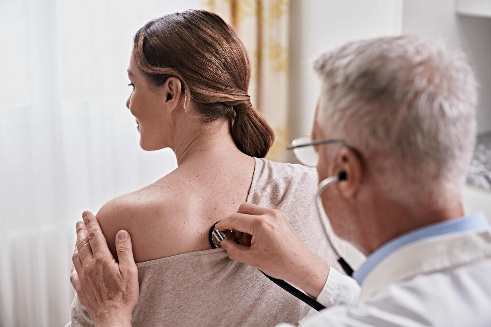 Ein Arzt hört eine Patientin im Rückenbereich ab.