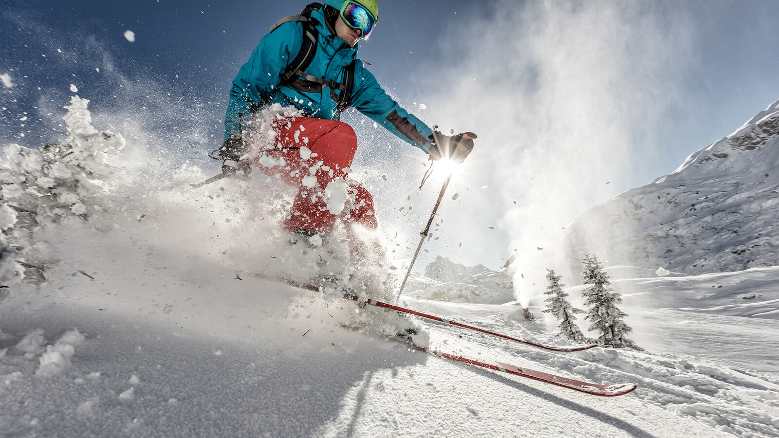 Ein Skifahrer fährt auf einen Skien durch den Tiefschnee, welcher entgegen spritzt. Hinter ihm sind Bäume und Berge zu sehen. Alles ist überdeckt mit Schnee. Diese Umgebung befindet sich in der Nähe vom Hotel Grand Resort Bad Ragaz, einem Superior Luxusresort in der Schweiz.