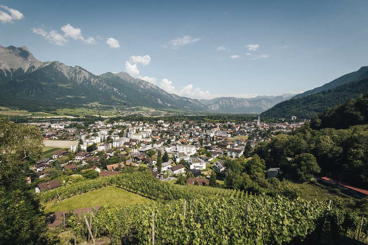 The village of Bad Ragaz can be seen from above. The mountains frame the village. Trees and fields can be seen everywhere.