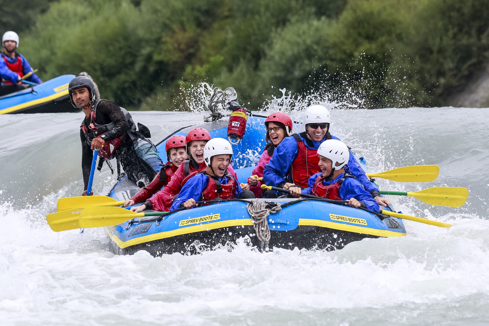 Eltern und Kinder fahren in einem Wildwasserboot durch strömendes Gewässer