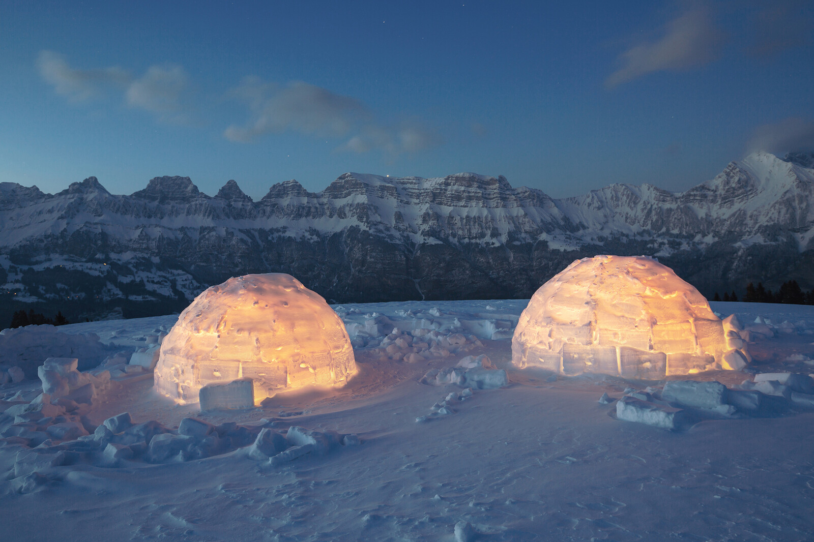 Zwei beleuchtete Iglus mit den schneebedeckten Churfirsten Bergen im Hintergrund.