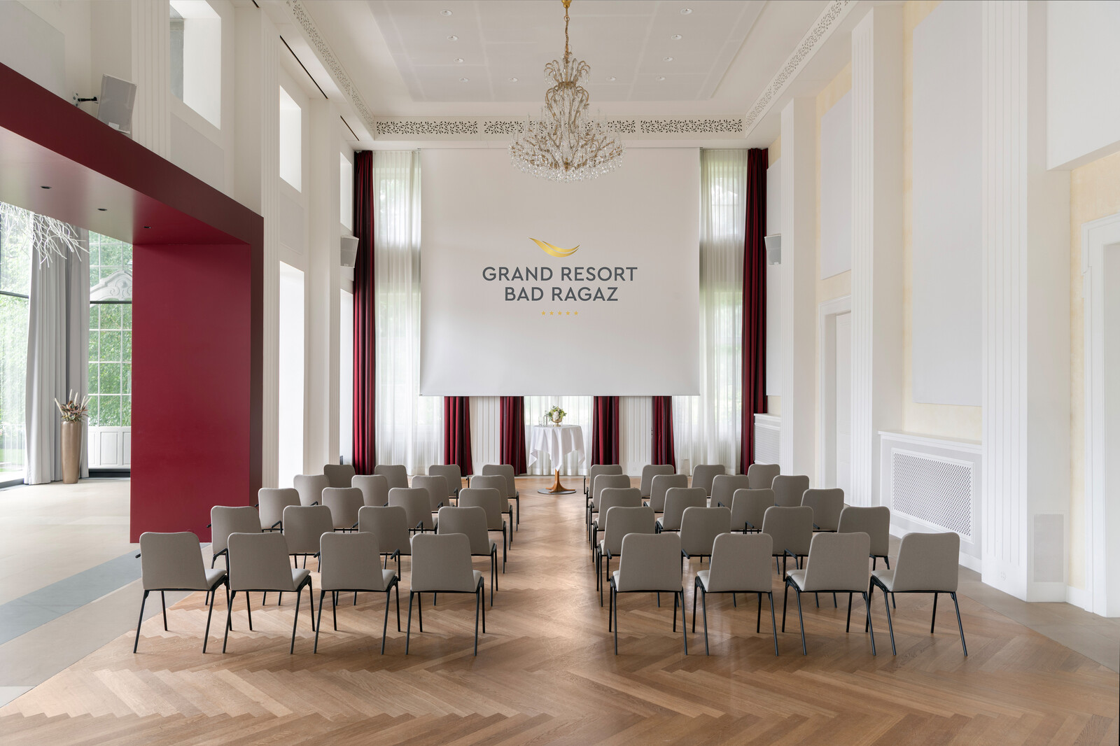 Eleganter Konferenzraum im Grand Resort Bad Ragaz mit beigen Stuhlreihen vor einem grossen Bildschirm. Die Atmosphäre ist formell und heiter.