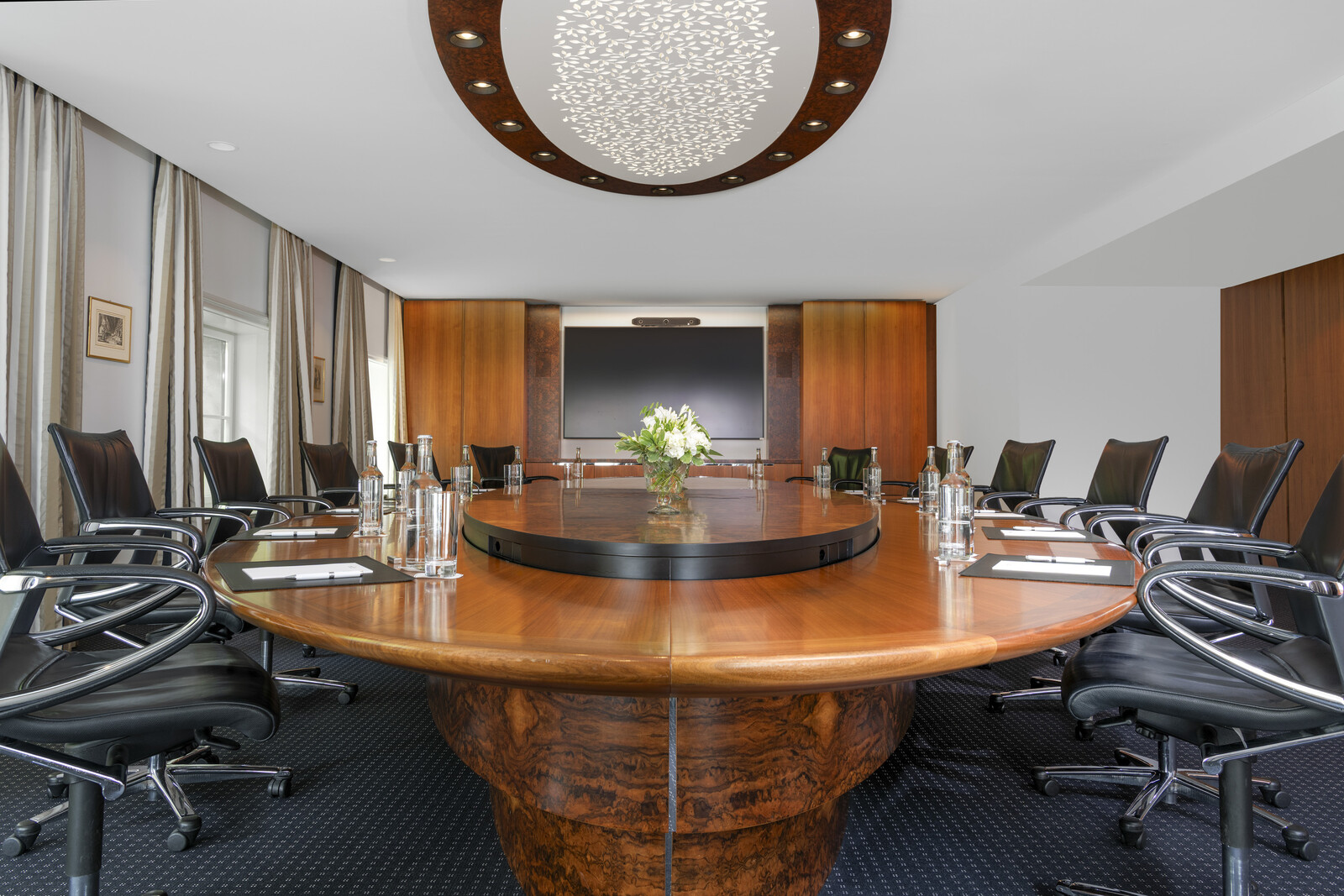 Im Kursaal ist der Board Room bereits für ein Meeting vorbereitet. Ein runder Holztisch befindet sich in der Mitte des Raumes. Stühle stehen um diesem herum. Über dem Tisch hängt ein grosser Kronleuchter. Die Fenster sind mit weissen Vorhängen verdeckt. Der Kursaal gehört zum Hotel Grand Resort Bad Ragaz, einem Superior Luxushotel in der Schweiz.