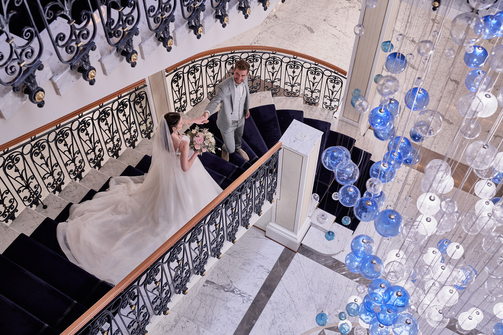 Die Braut schreitet in ihrem weissen Kleid die Treppen des Grand Hotel Quellenhof hinab. Ihr Bräutigam erwartet sie bereits auf den untersten Stufen. Das Hotel Quellenhof gehört zum Grand Resort Bad Ragaz, einem Superior Luxushotel in der Schweiz.