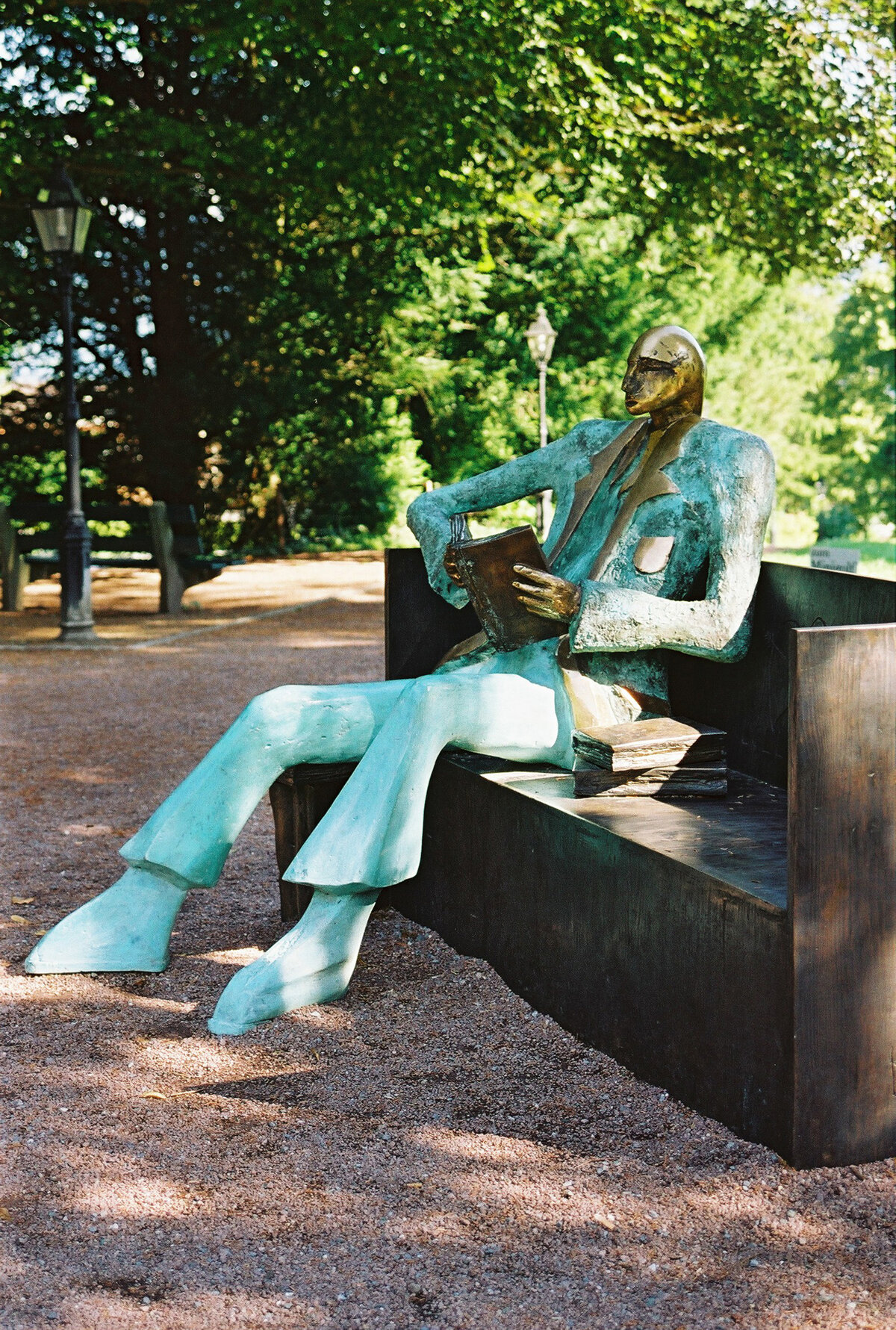 Eine Statue die einen Mann darstellt der auf einer Bank sitzt. Gebaut wurde Sie von dem Künstler Kurt Laurenz Metzler. Die Statue besteht aus einer Mischung aus Stein und Stahl. Kopf und Hände sind golden. Die Statue sitzt auf einer Bank aus Stagl und liest ein Buch das ebenfalls aus Stahl besteht. neben ihm sind zwei weitere Bücher.