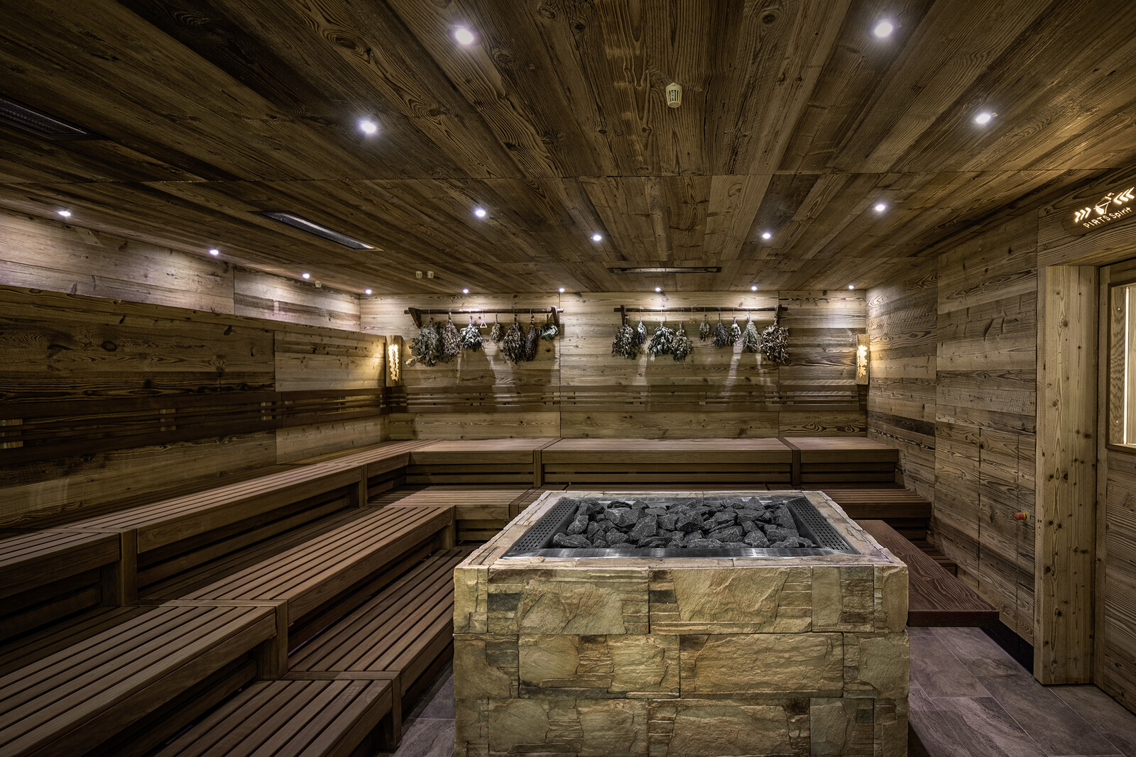 The sauna is made of wood. There is an oven in the middle of the room. Small lamps hang from the ceiling, making the sauna look like a starry sky. The whole thing is located in the wellness hotel Grand Resort Bad Ragaz, a superior luxury hotel in Switzerland.