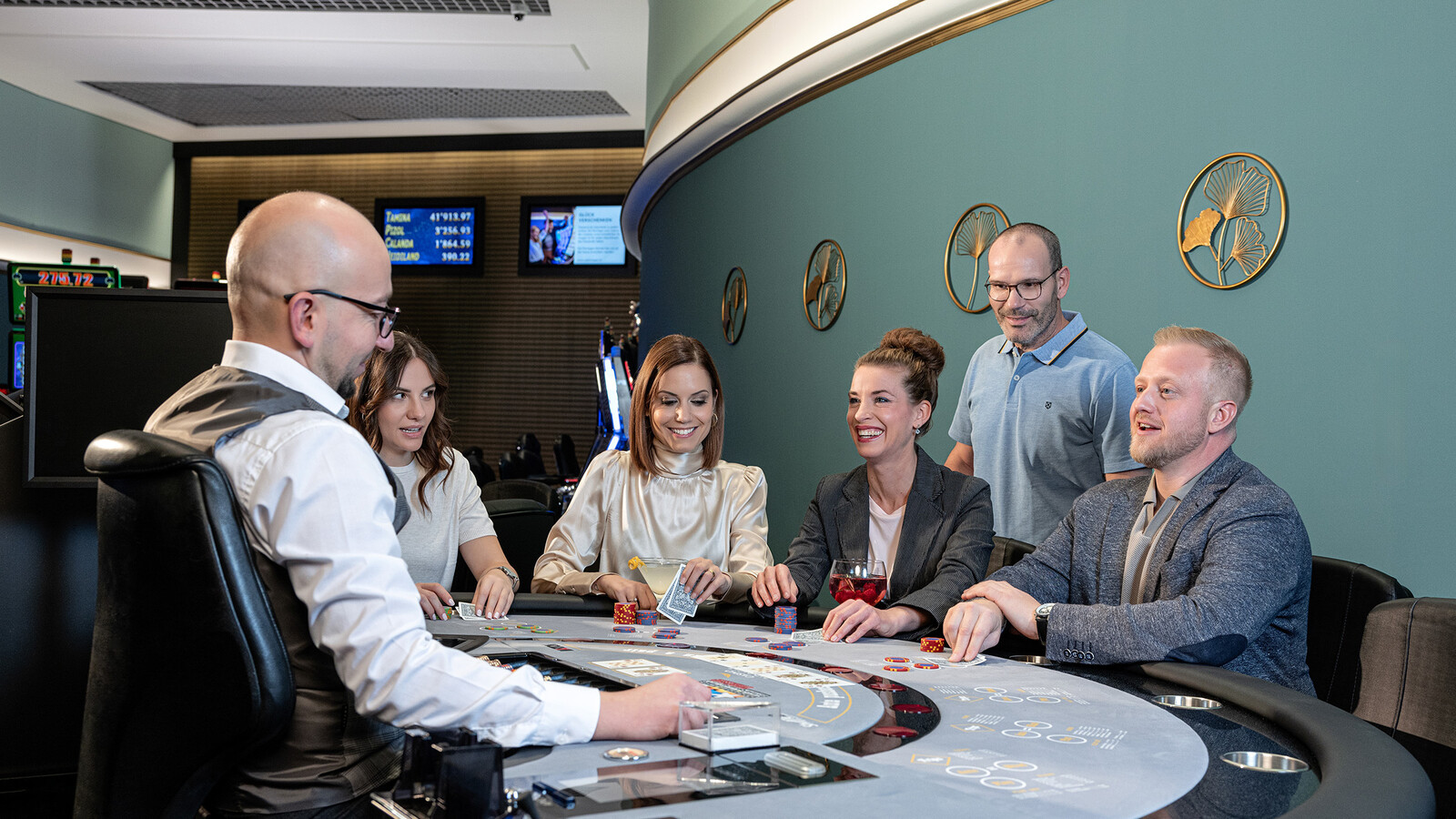Eine Gruppe von fünf Personen spielt Blackjack an einem Casinotisch im Casino Bad Ragaz, angeleitet von einem Geber mit Weste.