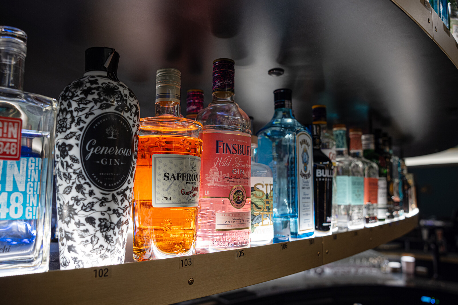 In der Goldem Wave Bar im Casino Bad Ragaz stehen verschiedene Gin-Flaschen in einem geschwungenen, hinterleuchteten Regal. Die Flaschen haben leuchtende Farben und einzigartige Etiketten,