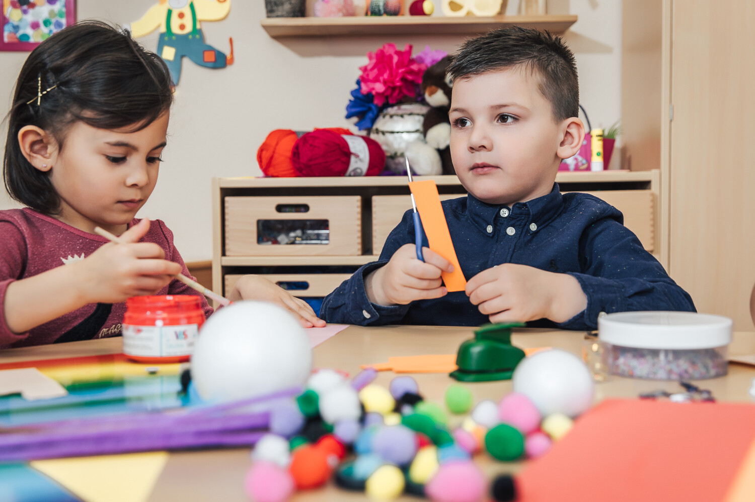 Ein Mädchen und ein Junge basteln am Basteltisch der Kinderbetreuung in der Kindervilla