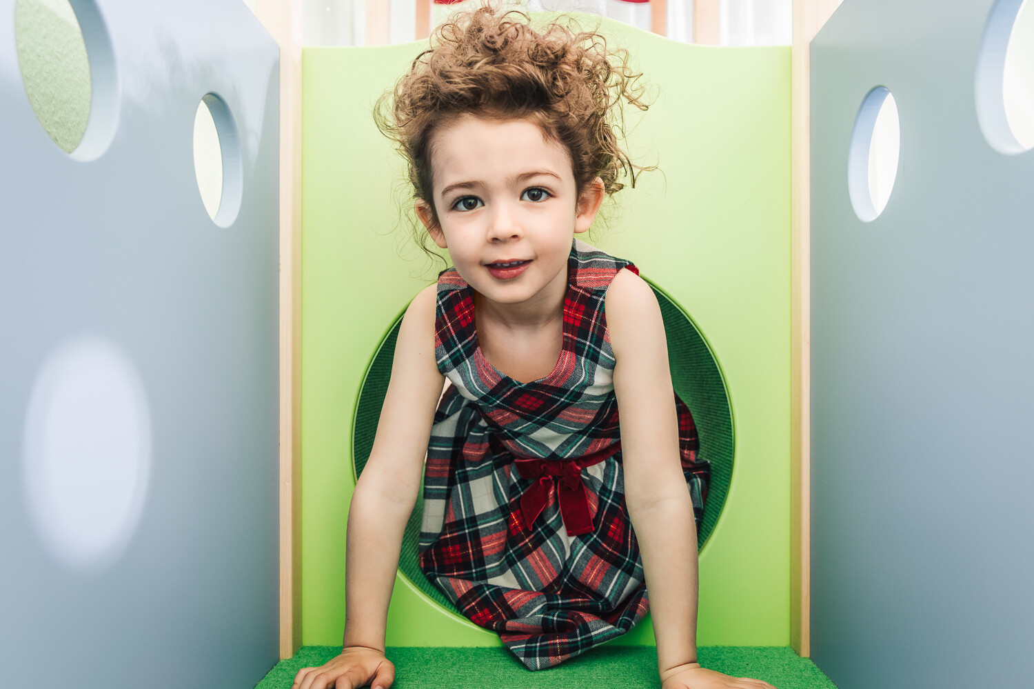 Ein Mädchen in rot-weiss kariertem Kleid klettert aus der grünen Röhre heraus und lacht in die Kamera. Die grüne Röhre befindet sich in dem Wellnesshotel Grand Resort Bad Ragaz, einem Superior Luxushotel in der Schweiz.