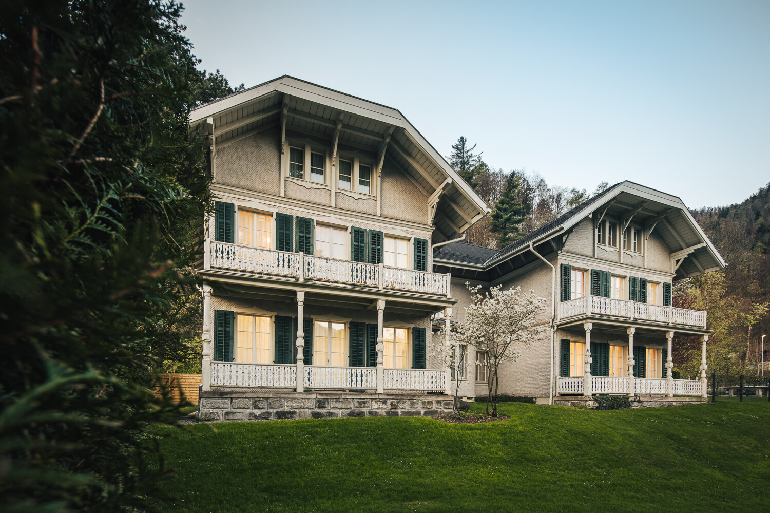 Die Kindervilla besteht aus zwei weissen Holzhäusern mit Terrasse. Die Storen sind dunkelgrün. Auf der linken Seite des Hauses steht eine grosse Tanne. Das Haus befindet sich auf einem kleinen Hügel hinter dem Wellnessresort Grand Resort Bad Ragaz. Das ist ein Superior Luxushotel in der Schweiz.