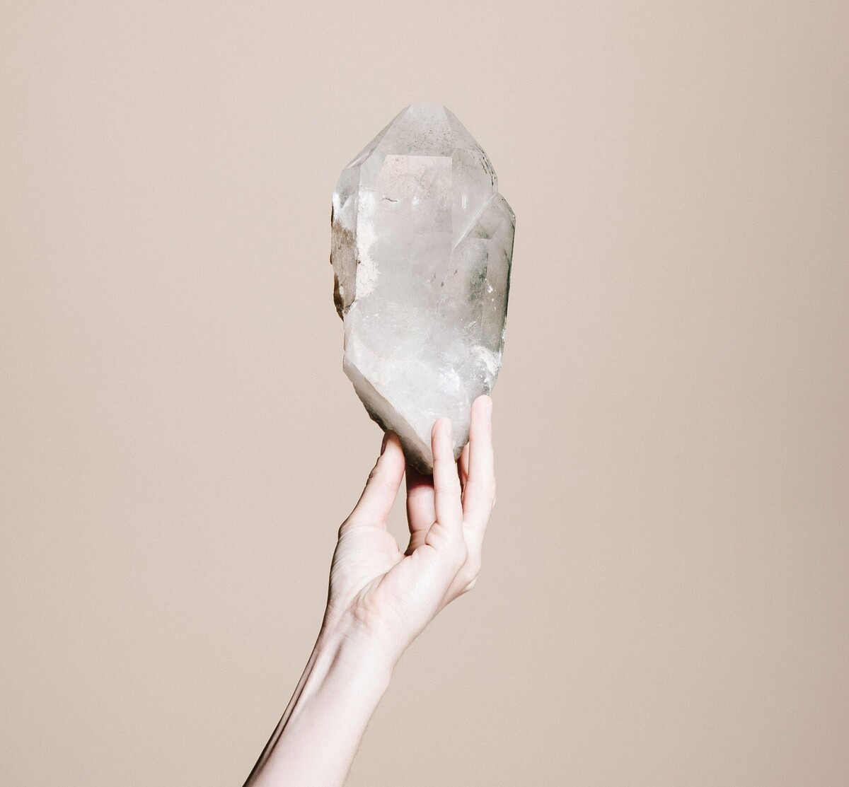 Hand hält Kristall in die Luft mit beigem Hintergrund