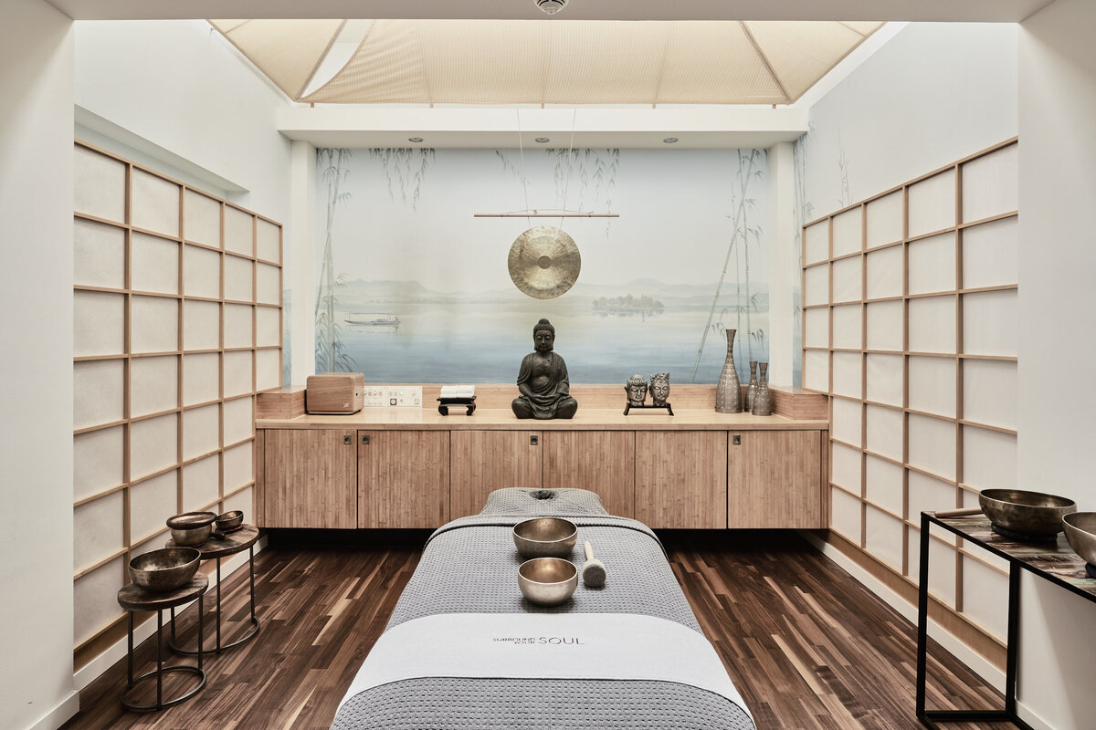 Eine graue Liege befindet sich in der Mitte des asiatischen Behandlungszimmers. Klangschalen liegen darauf. Das Behandlungszimmer befindet sich im Thermal Spa, welcher sich im Wellnessresort Grand Resort Bad Ragaz befindet. Dies ist ein Superior Luxushotel in der Schweiz.