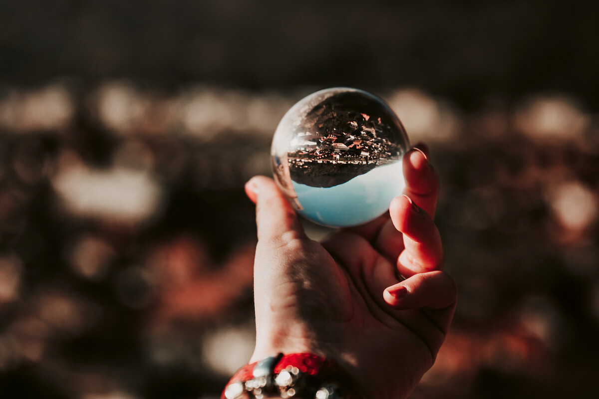 Eine Hand hält vor eine verschwommene Stadt nachts einen silbernen Ball in die Kamera. In dem Ball spiegelt sich die Stadt wieder und sieht aus wie bei Tageslicht.