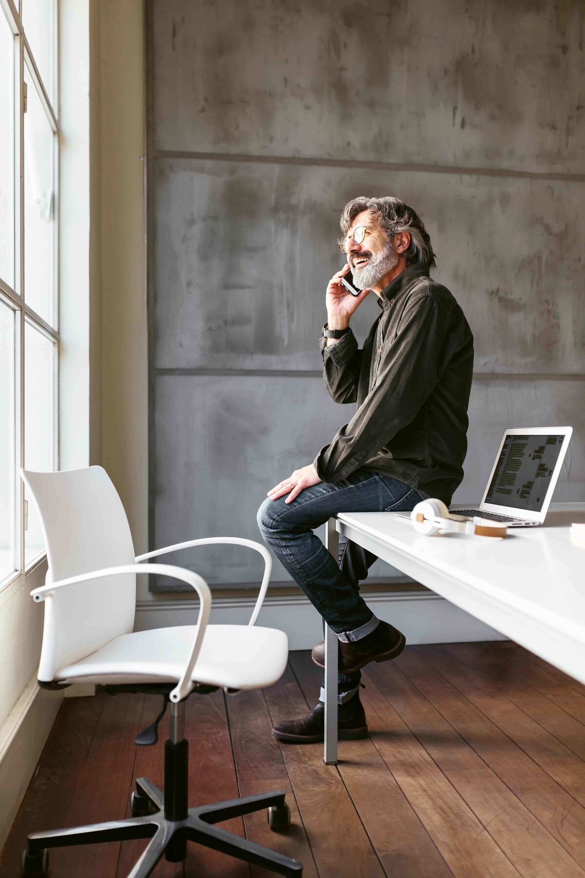 Ein Mann sitzt im Büro auf seinem Schreibtisch und schaut beim Telefonieren aus dem Fenster.