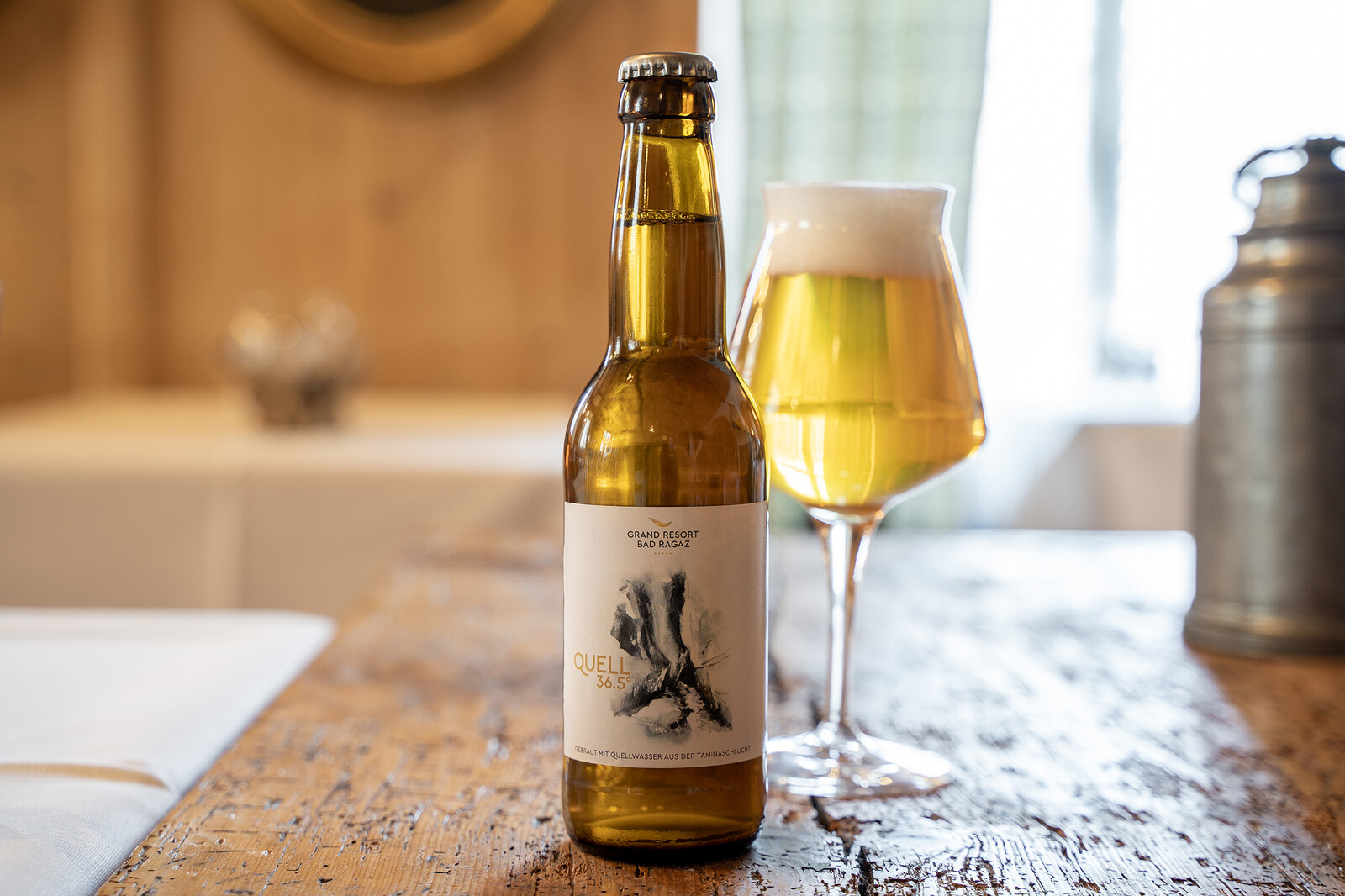 Eine Nahaufnahme der Quell 36.5 Flasche und einem Glas Bier daneben.