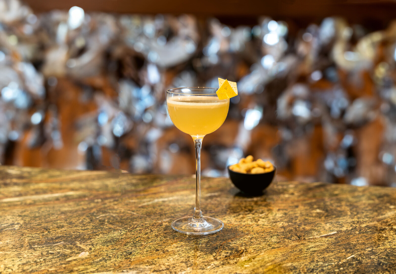 Blick auf den Bees & Knees des verve by sven. Der alkoholfreie Drink ist gelb und wurde in einer Cocktailschale mit einer Zitronenzeste angerichtet.